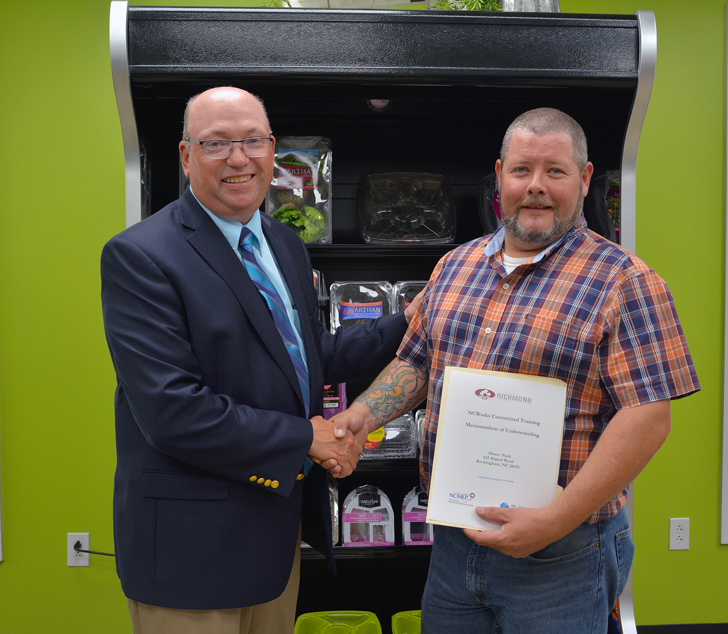 Dr. Dale McInnis stands with Lowell Rogers, plant manager, with a contract for customized training