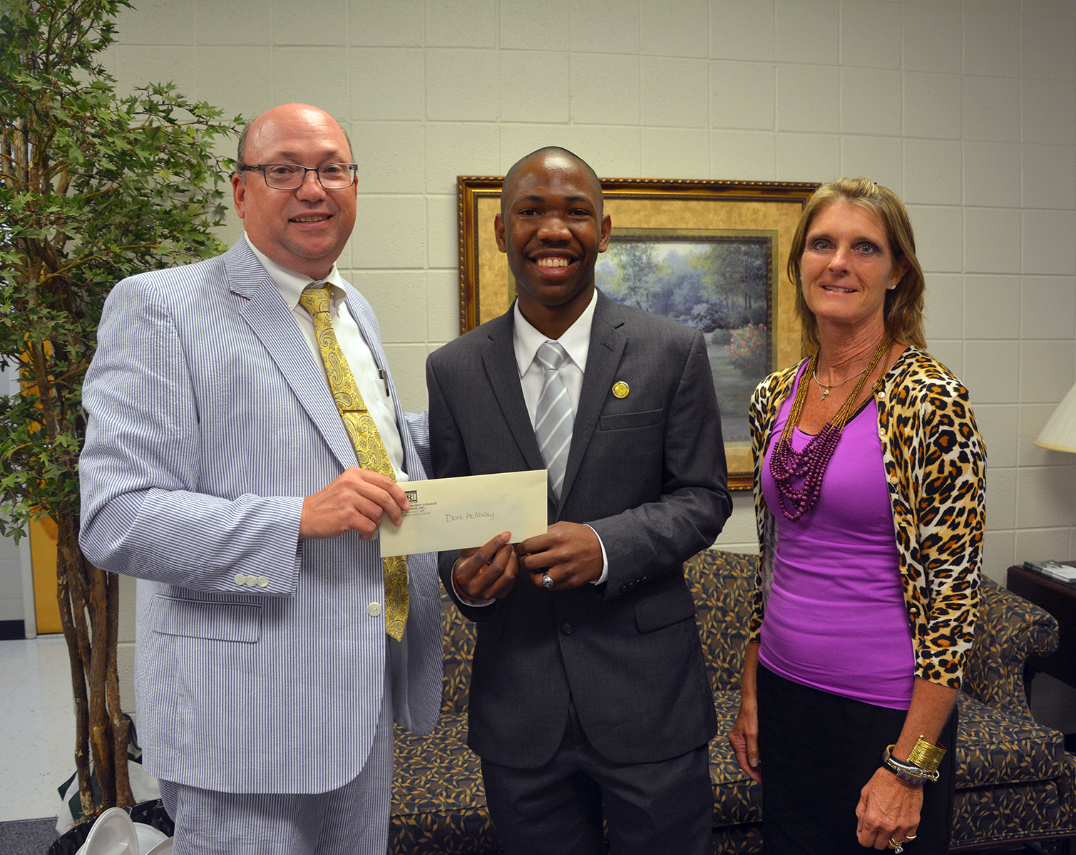 Doni Holloway, a Scotland Early College graduate, won first place in a Richmond Community College essay contest. He is congratulated by RCC President Dr. Dale McInnis and Board of Trustees Chair Claudia Robinette as he accepts his cash prize of $100.