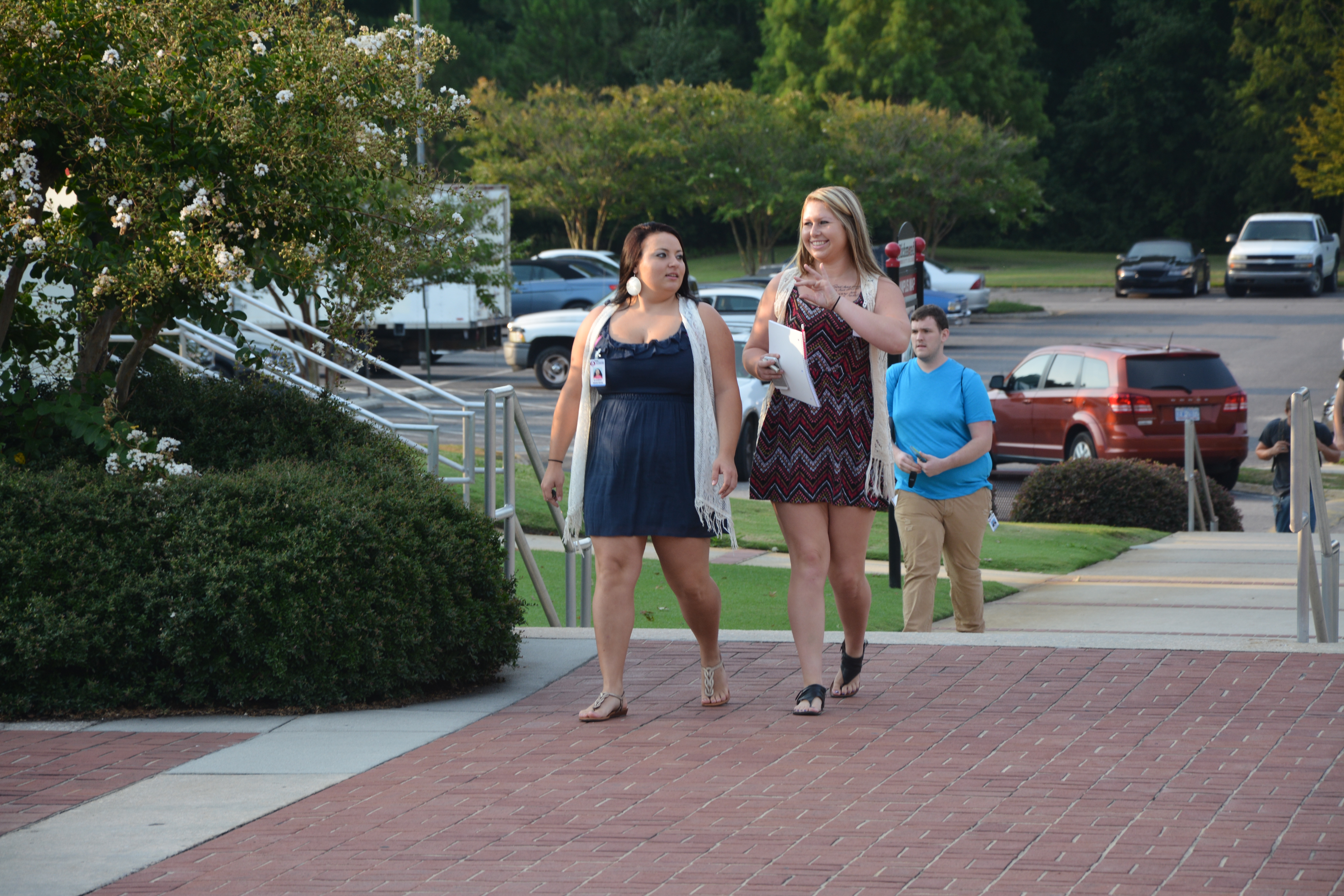 Two female students walk up the steps of the main campus. One student is waving to another student