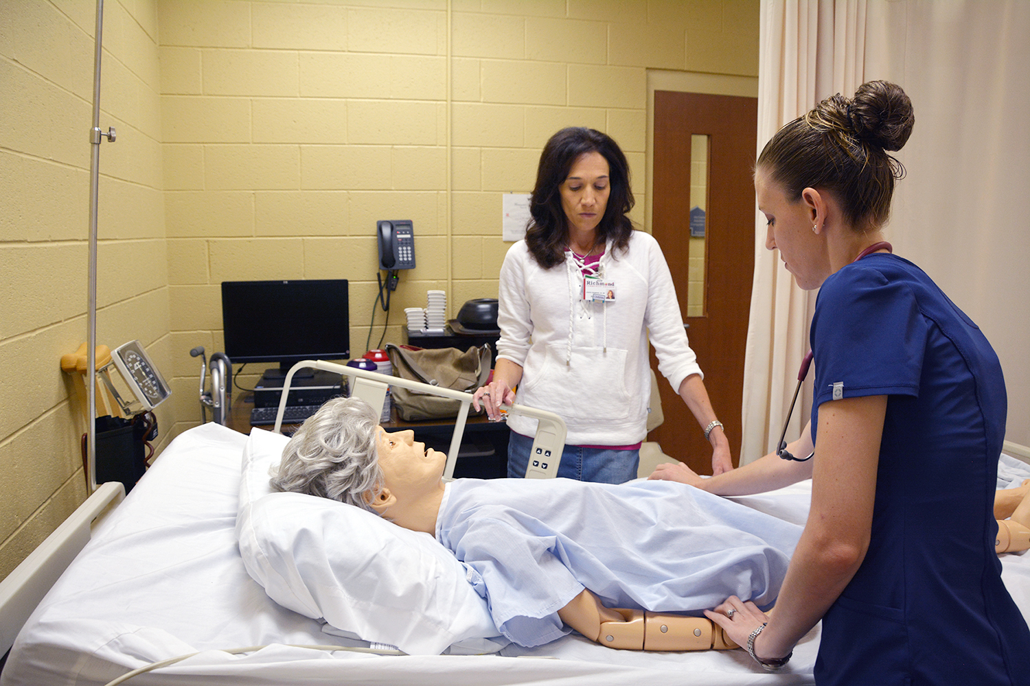 Nursing student working with an instructor and a mannequin in nursing lab
