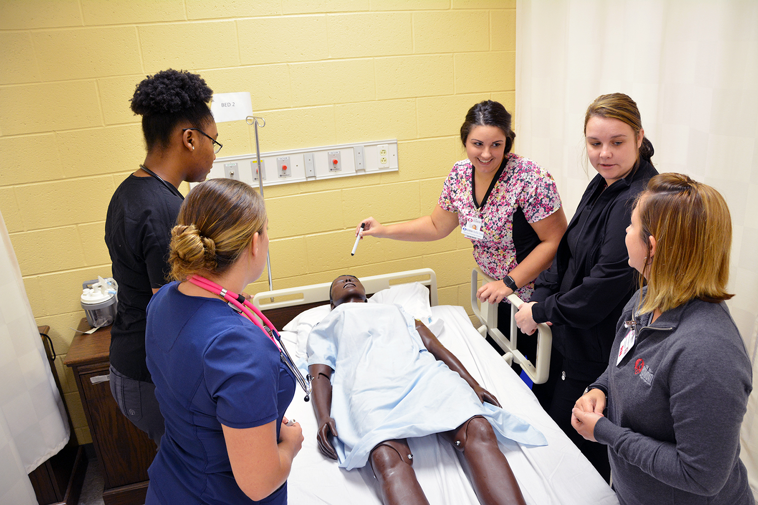 Practical Nursing students around a bed in the nursing lab