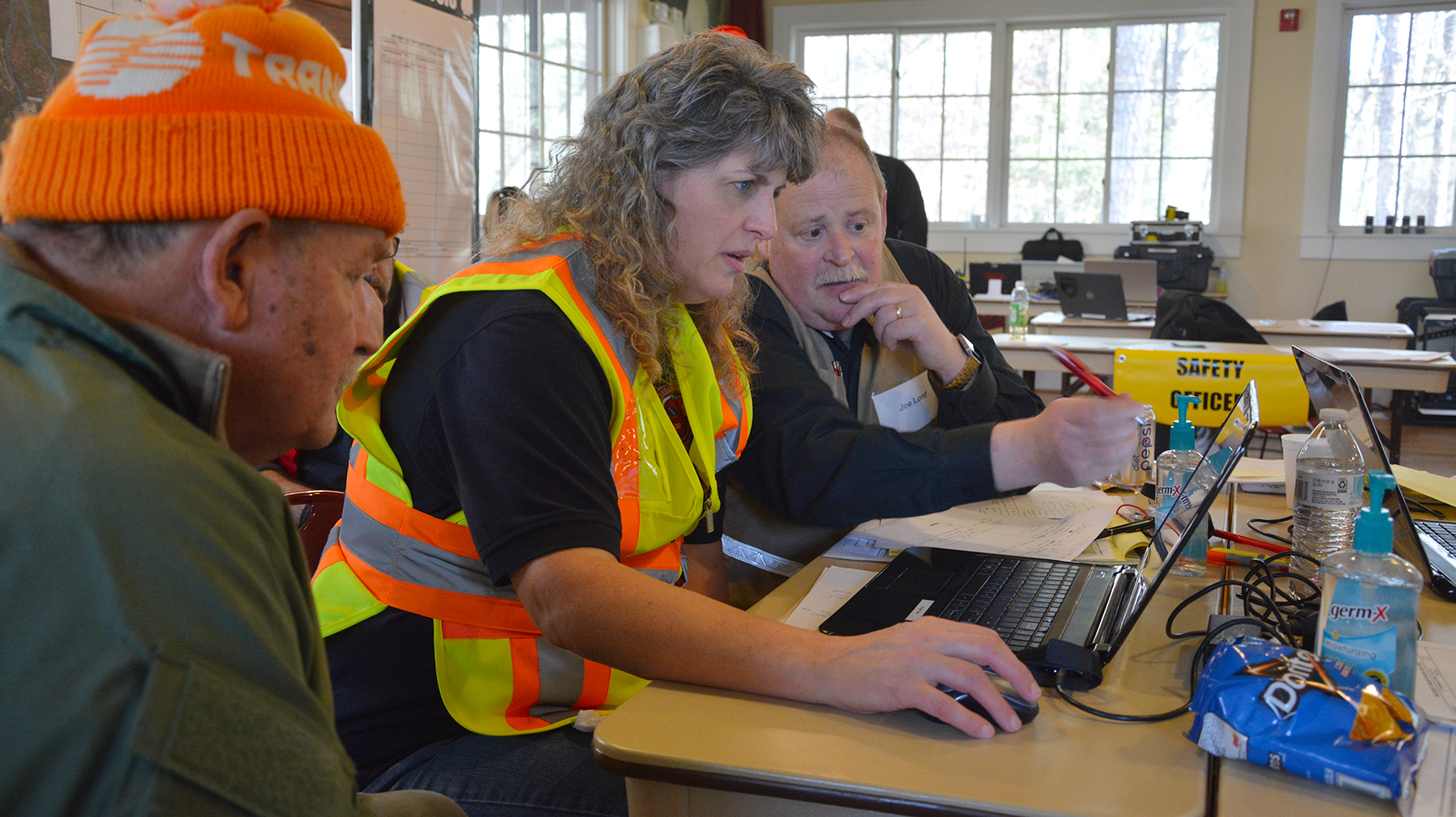 Three members of the incident management team look at a computer with in the search and rescue command center