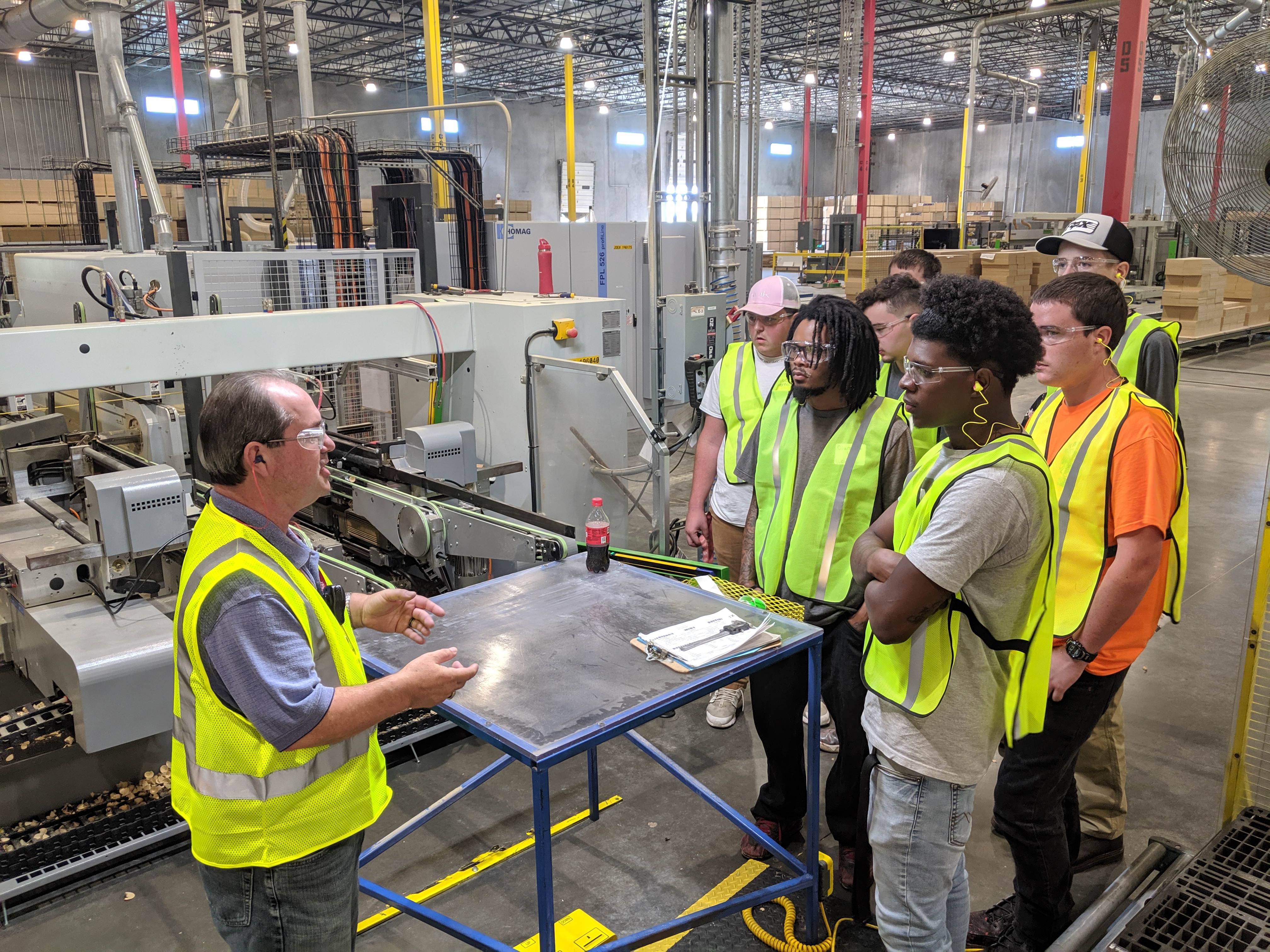 Students stand listening to a plant employee talk about the manufacturing process