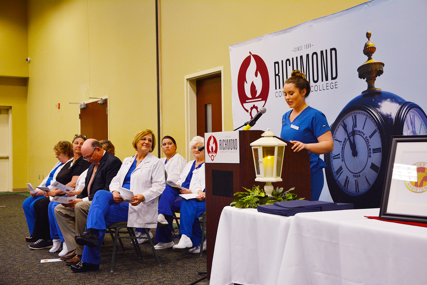 Nursing Assistant student Carolina Walker stands at podium addressing classmates during pinning ceremony