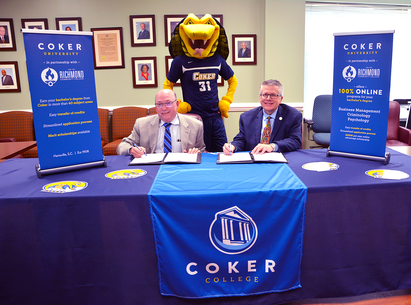 Dr. McInnis and Dr. Wyatt sign the documents to create bridge program with Coker's mascot, Striker, standing behind them.