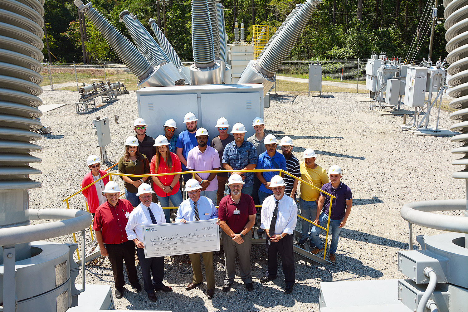 A representative from Duke Energy and Richmond Community College students, faculty and staff stand in the substation holding a big check.