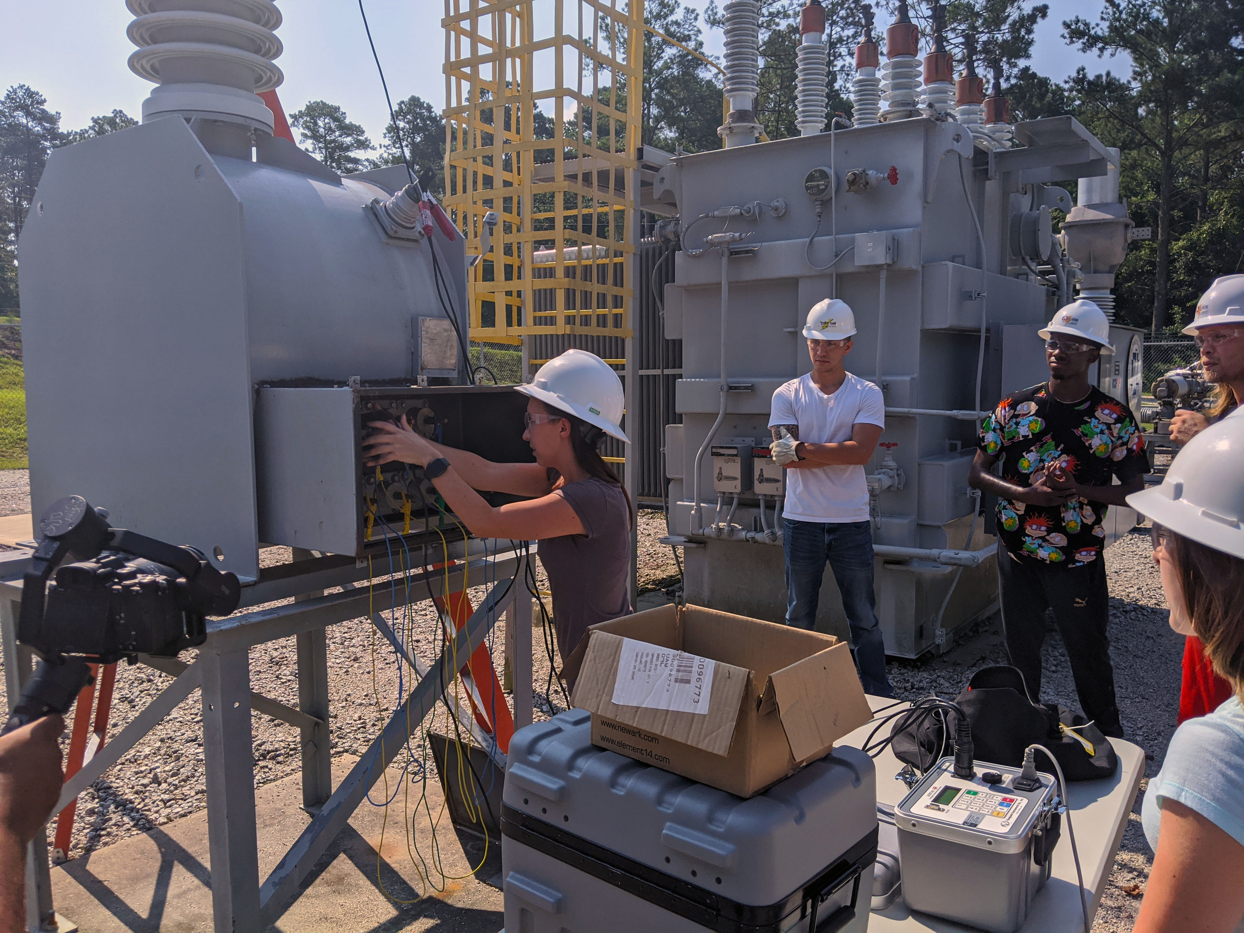 Students stand in the substation and work on testing equipment