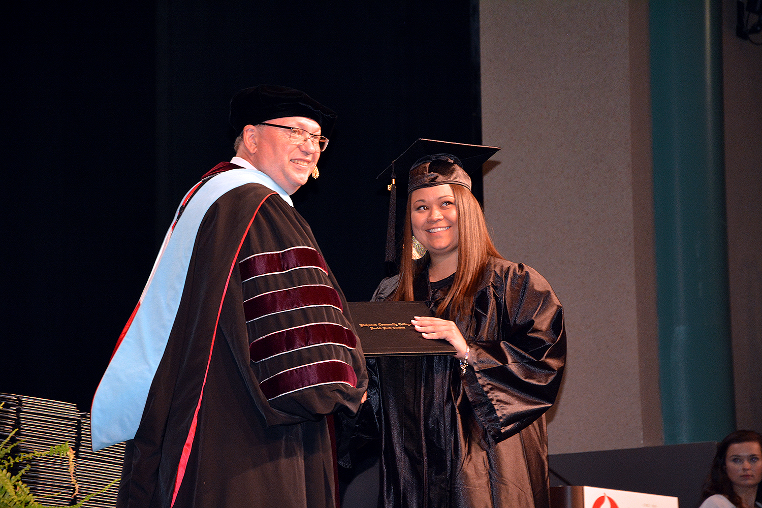 Graduate accepts a diploma and smiles for the camera with Dr. McInnis