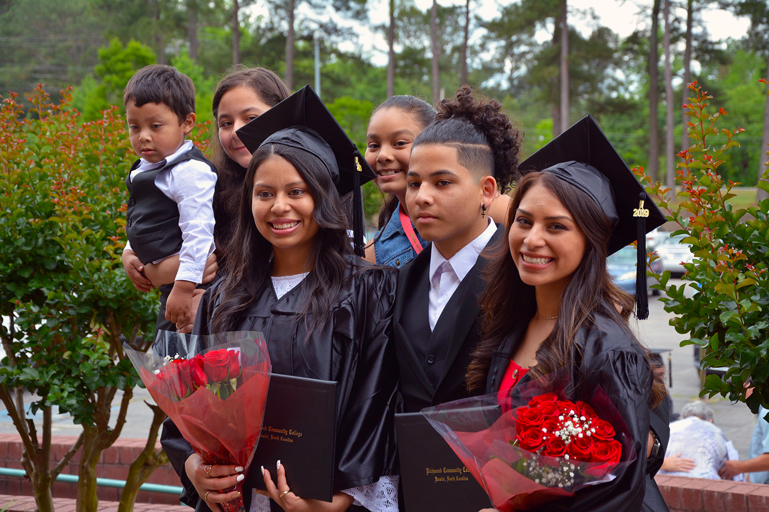 Two graduates stand with family members after the graduation ceremony