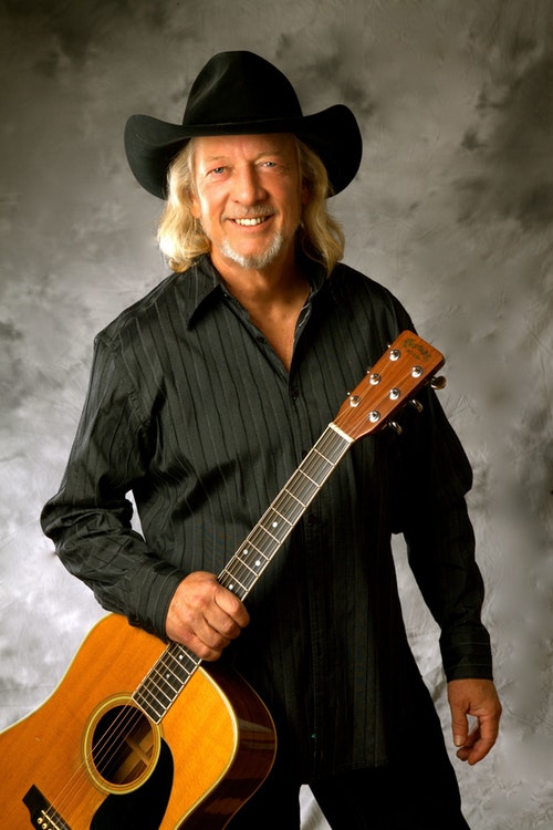 Photo of John Anderson in black cowboy hat holding a guitar