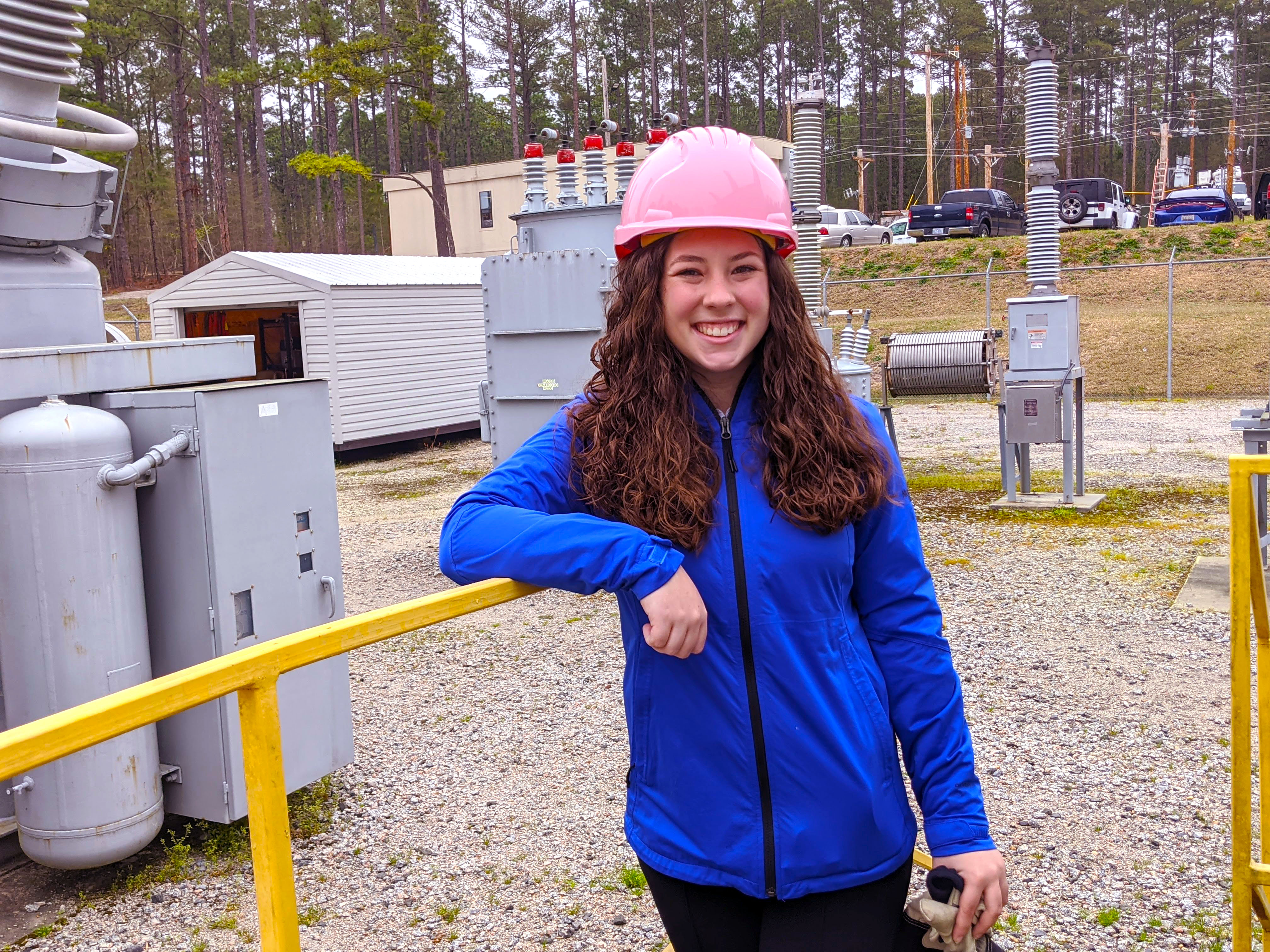 Lauren Humann wears a hard hat and stands in the substation on campus