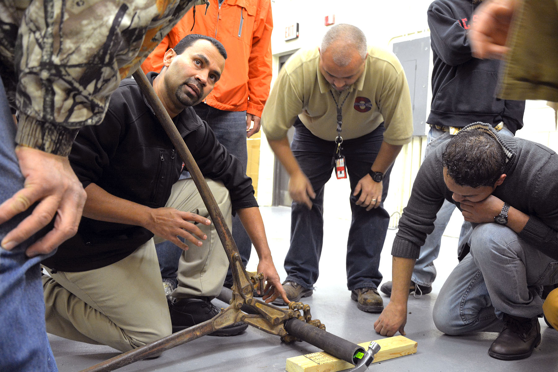 An instructor kneels by a pipe and talks to students about plumbing