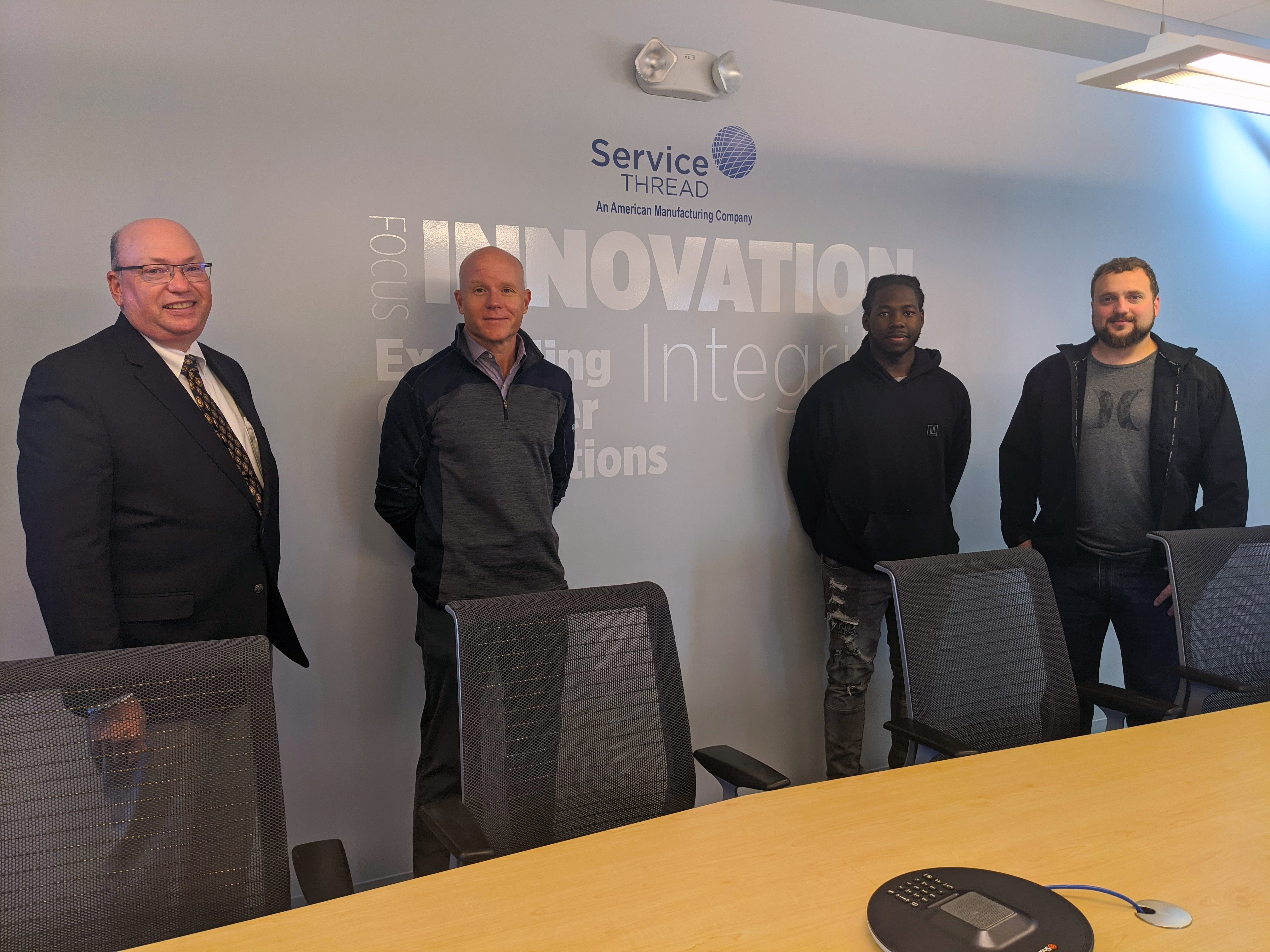 College President stands with CEO of Service Thread and two employees in a conference room