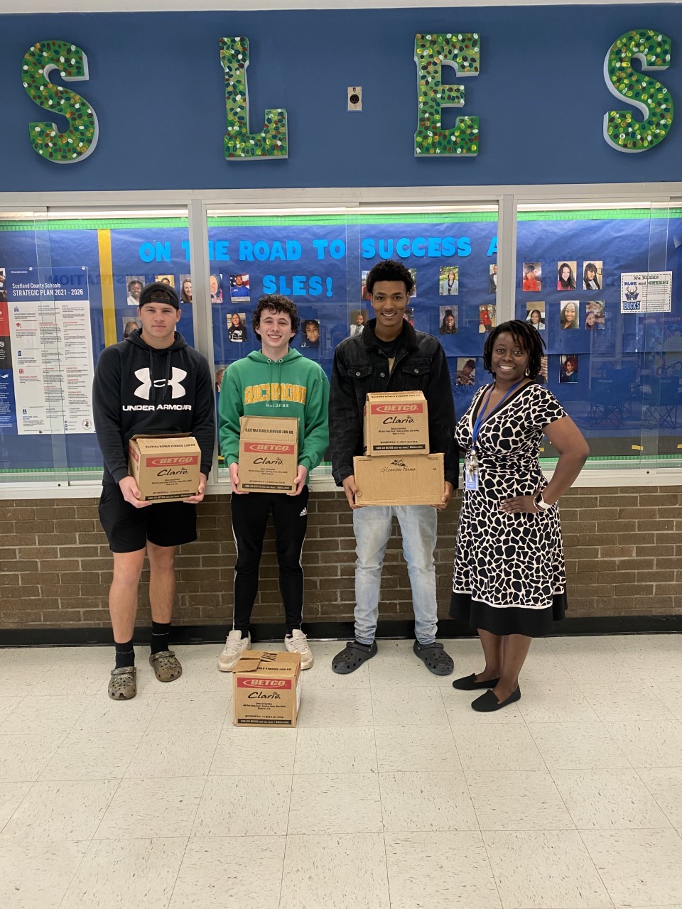 Students stand with the school principal holding meal boxes