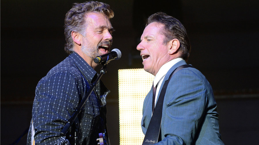 John Schneider and Tom Wopat sing together on stage in promo photo.