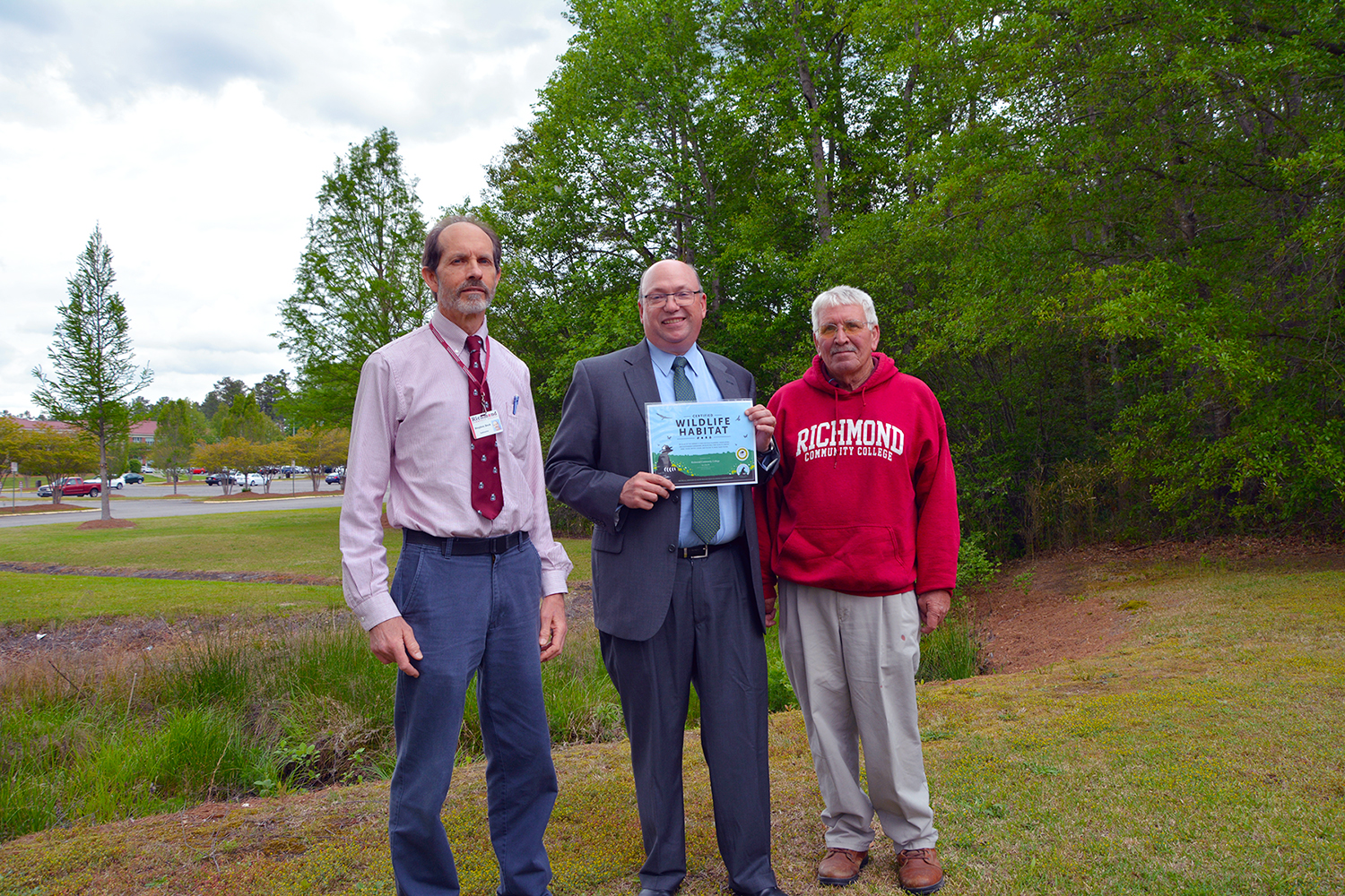 College officials stand near the creek on the campus holding the Wildlife Habitat certification
