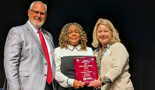 Evonne Moore holds an award for being an outstanding alumni of RichmondCC with two college leaders standing with her.