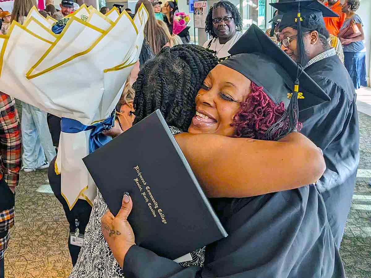 Adult High School graduate holds her diploma hugging a family member