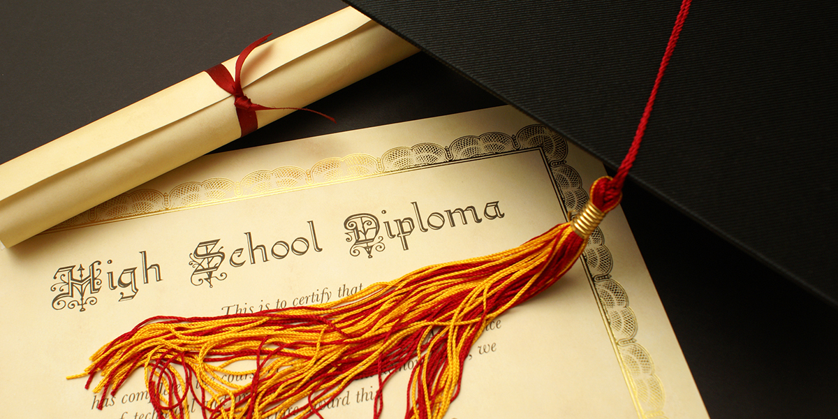High school diploma with cap lying on the paper diploma