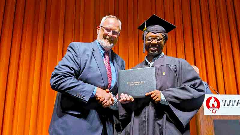 College President Barbee hands a diploma to an Adult Education graduate on stage of the Cole Auditorium.