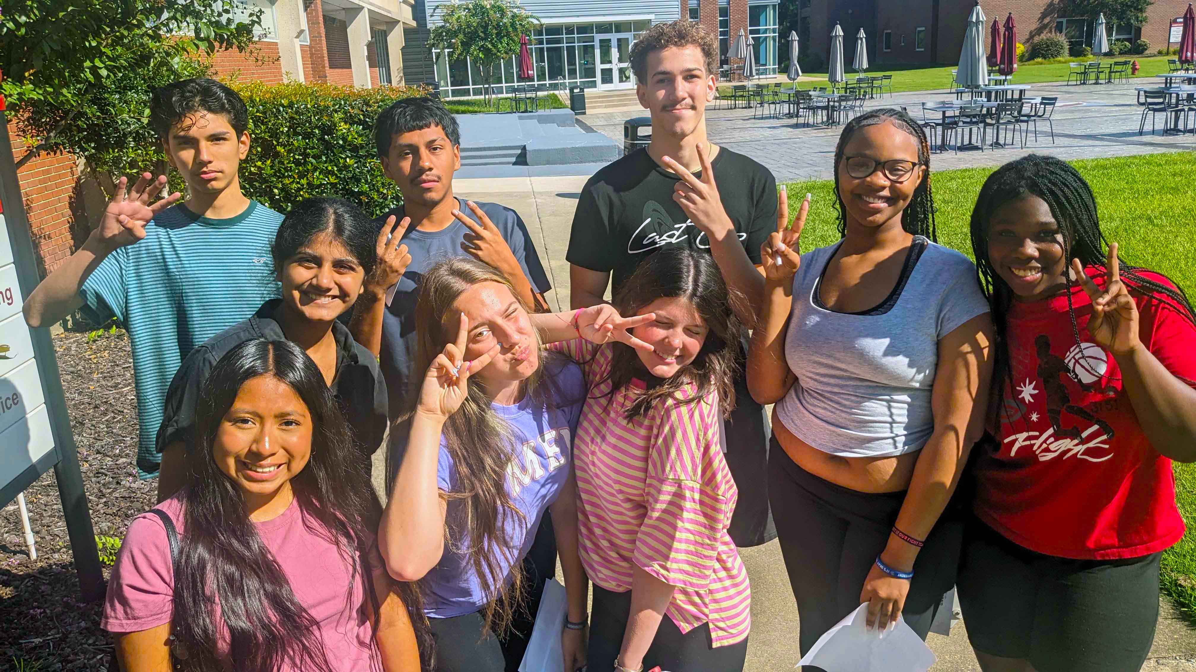 Dual enrollment high school students stand in a group making faces and holding up fingers