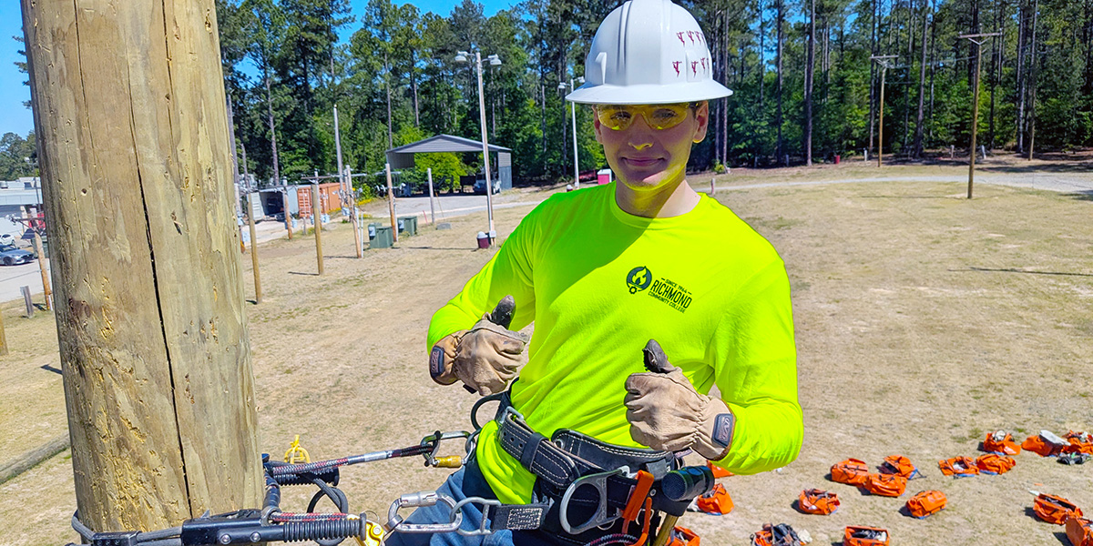 Lineman student giving thumbs up while balanced on the side of a powerline pole