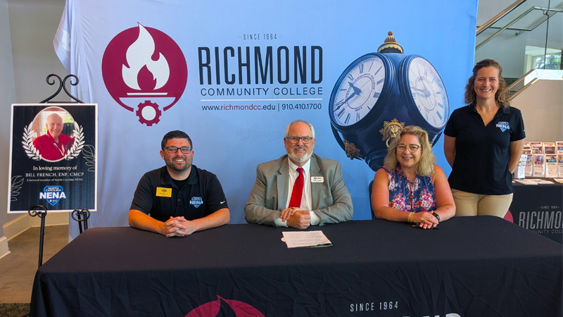 College leaders and 911 leaders sit at table signing a scholarship