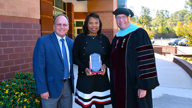 Dr. Yolanda VanRiel holding her award while standing beside Dr. Schuler and Dr. McInnis