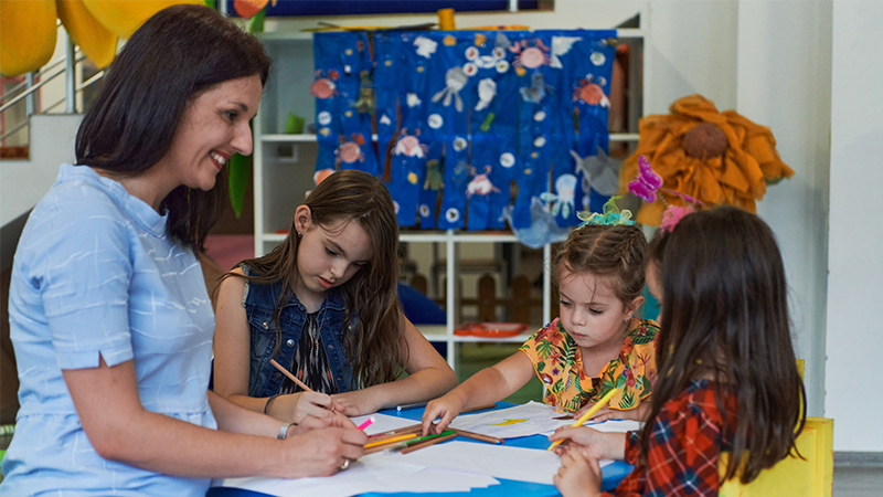 Teacher works with kindergarten students at a desk