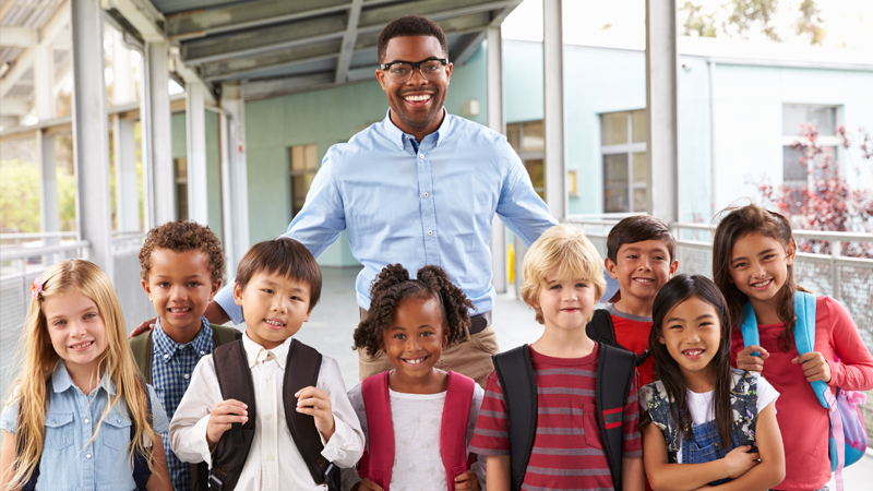 Educator stands with several children outside on a school campus