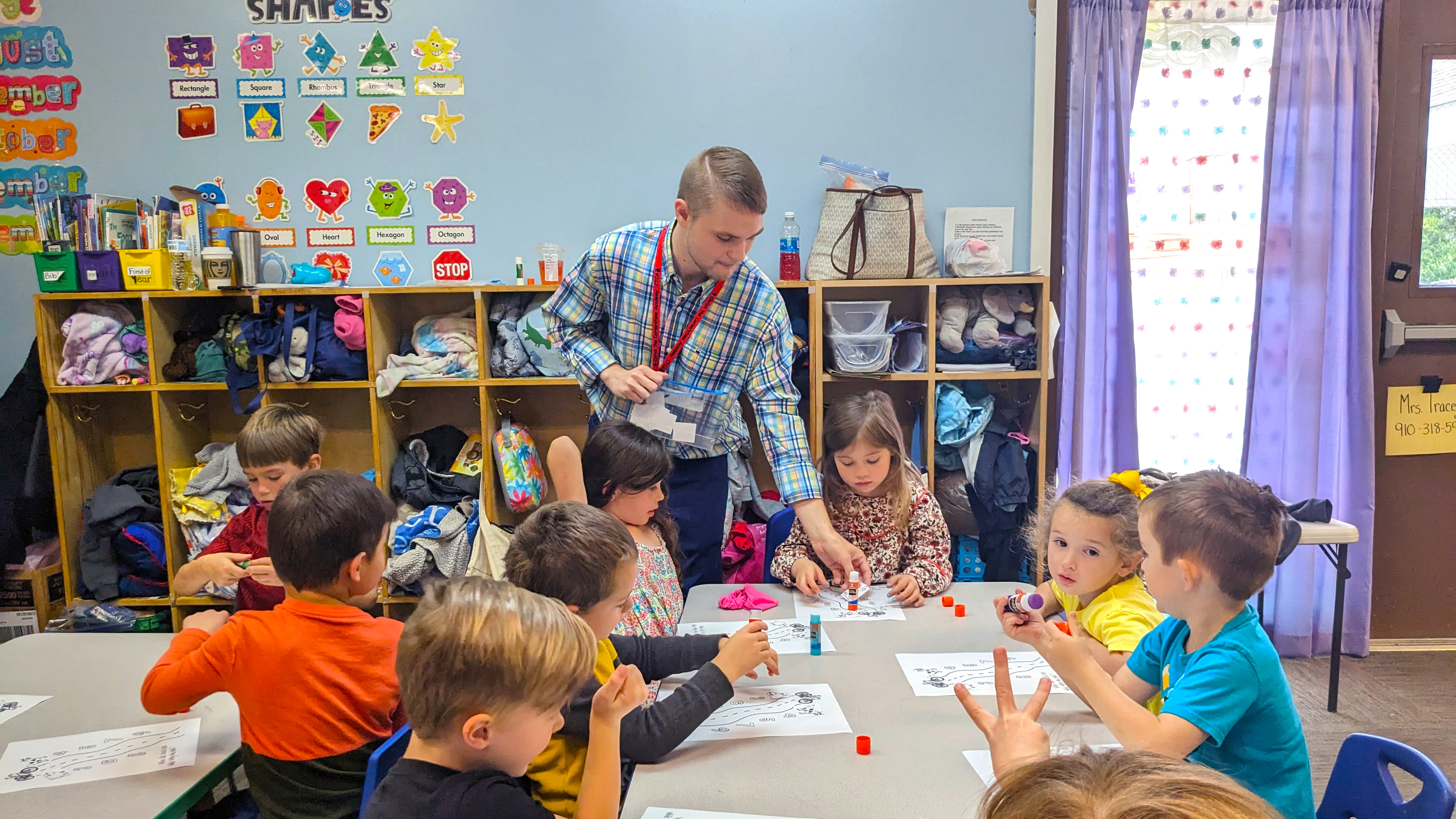 Teacher passes out papers to children in a classroom.