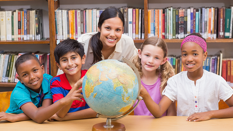 Teacher shows 4 students a globe on a desk