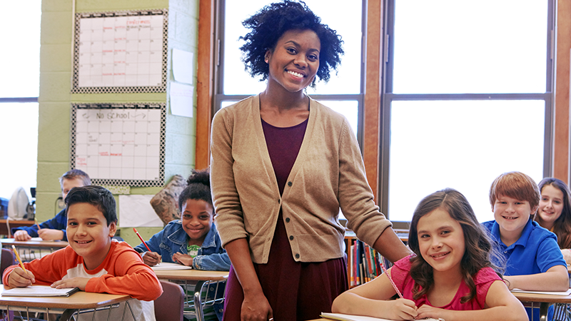 Teacher stands smiling in a classroom of students