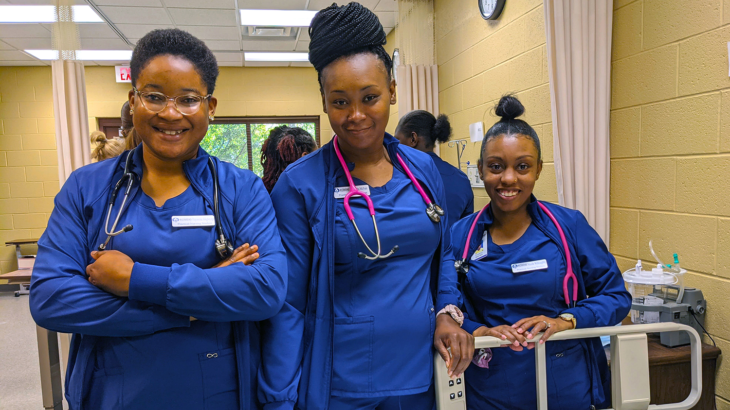Three nursing students wear their uniforms and smile at the camera.