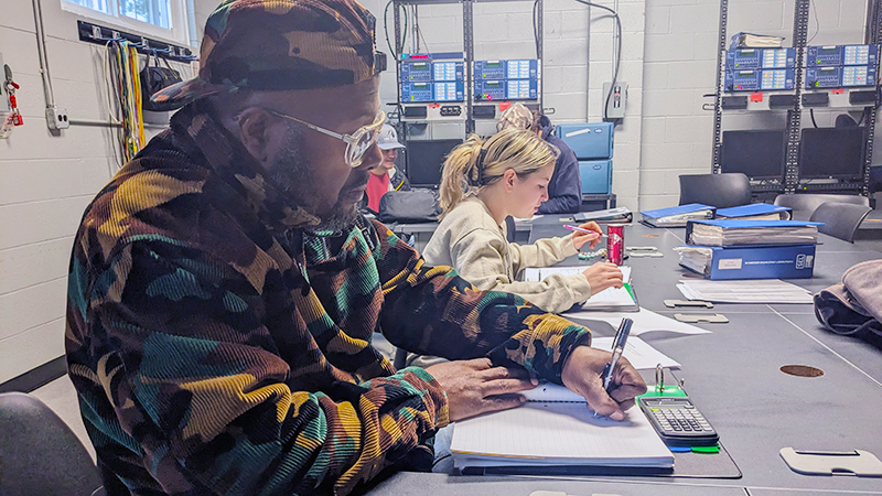 A student sits at a desk with a notebook in front of him.