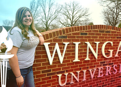 Early College graduate Lisa Hogan who used her Associate in Science degree earned from Richmond Community College to transfer to Wingate University stands beside the Wingate University sign