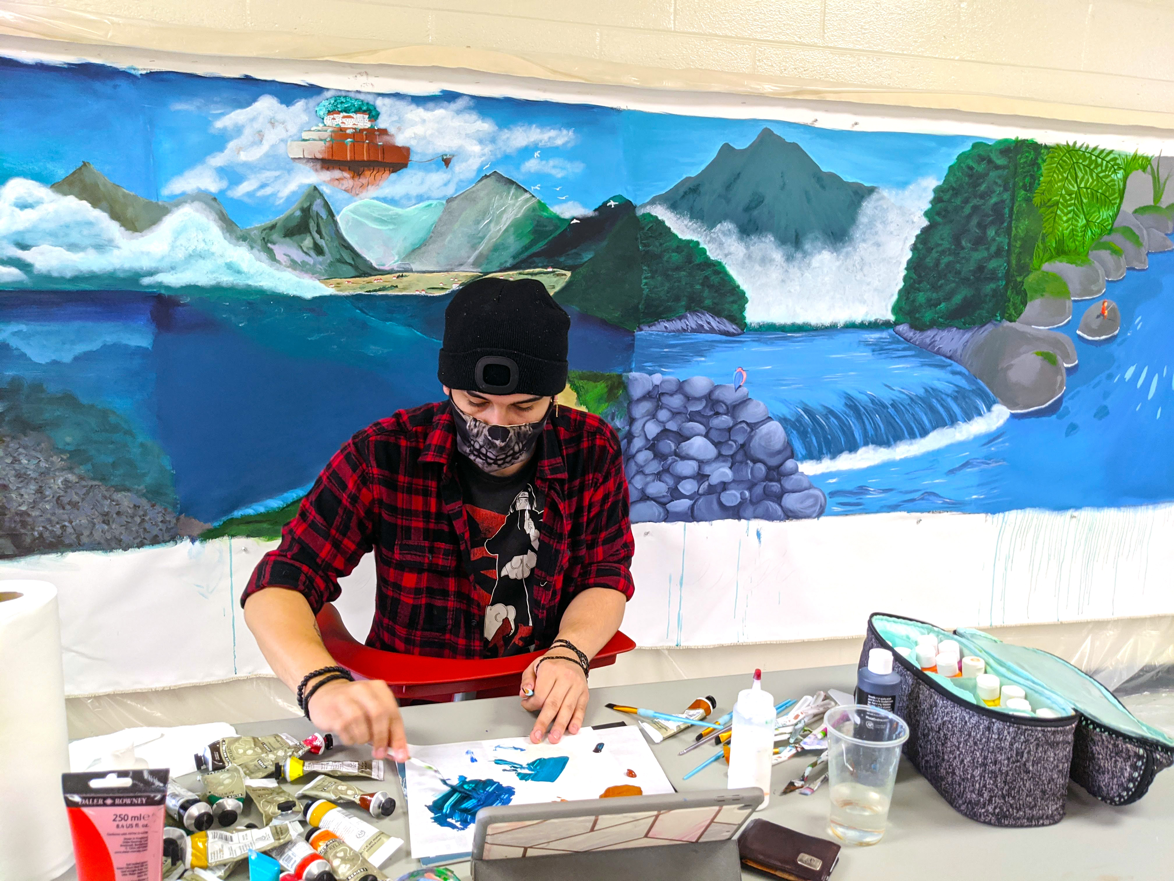 Photo of student mixing paint in front of a mural