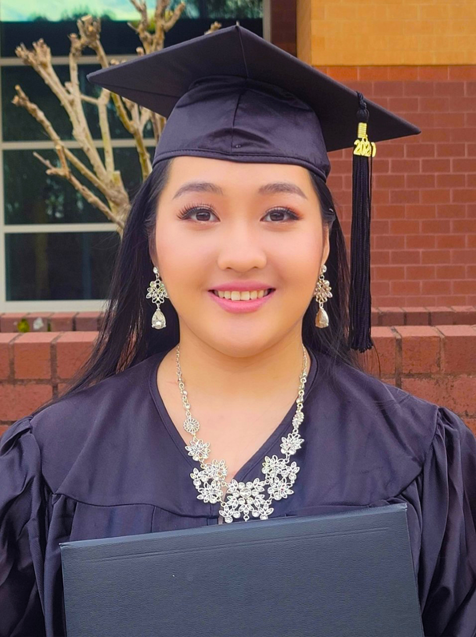 April Xiong stands in her cap and gown holding her diploma.