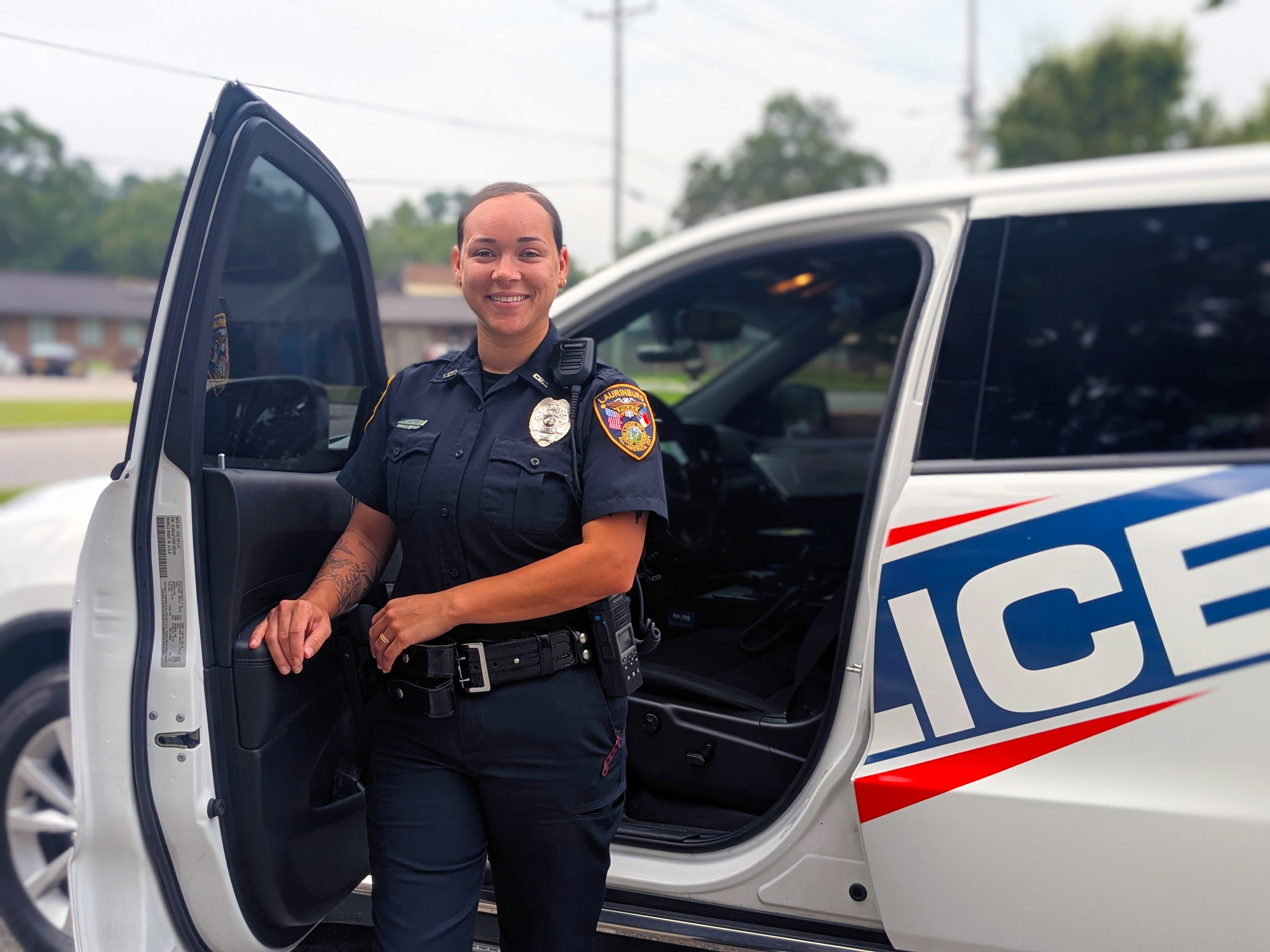 Woman police officers stands next to her police vehicle.