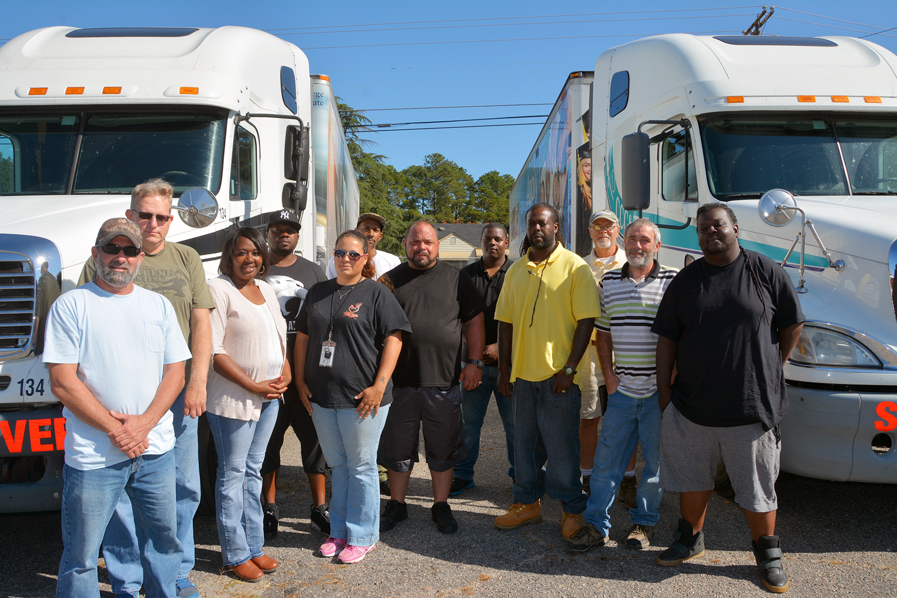 A group of students in the truck driver training program stand beside two 18-wheelers