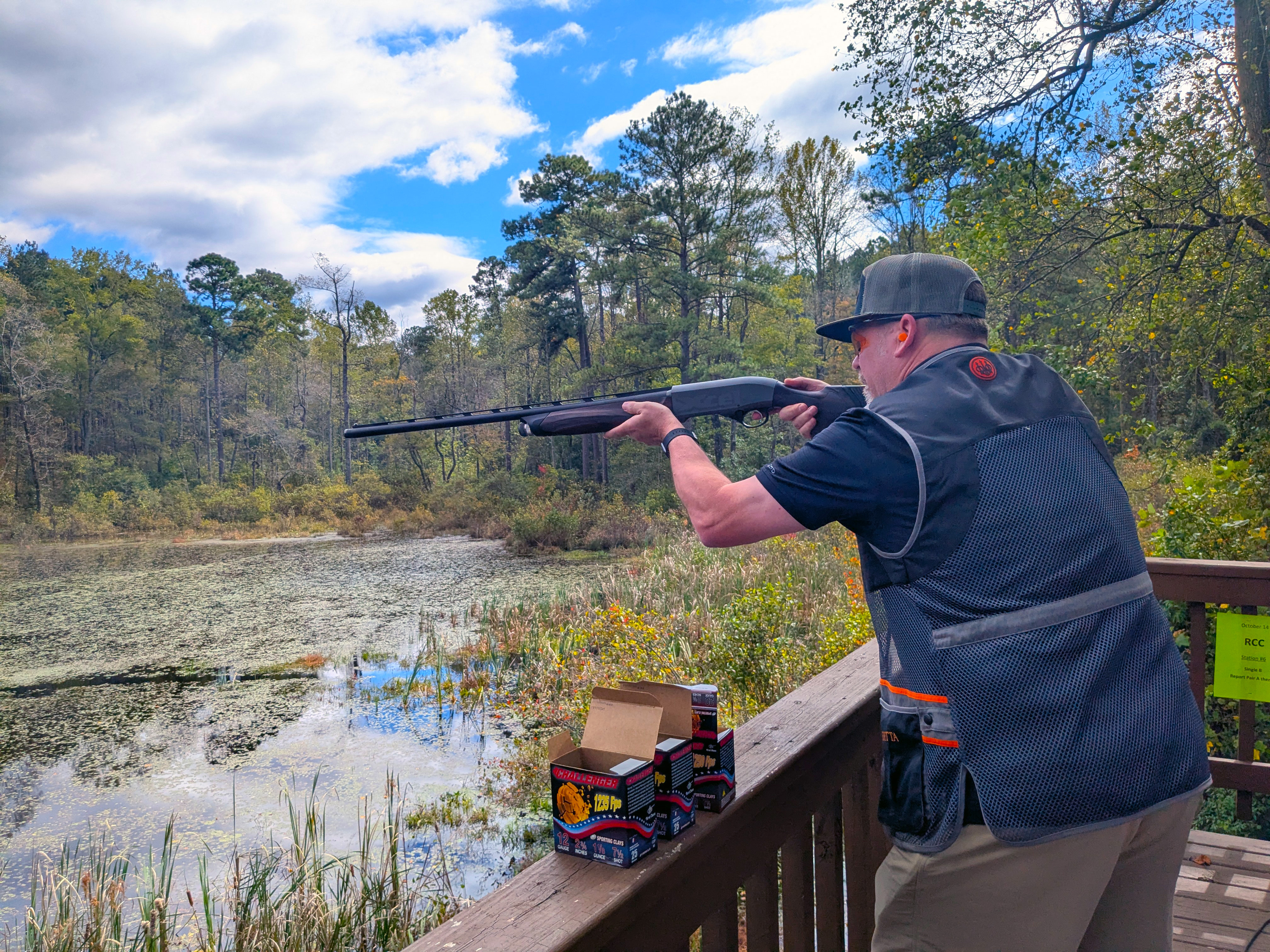 Clay shoot participant aiming a gun over a lake.
