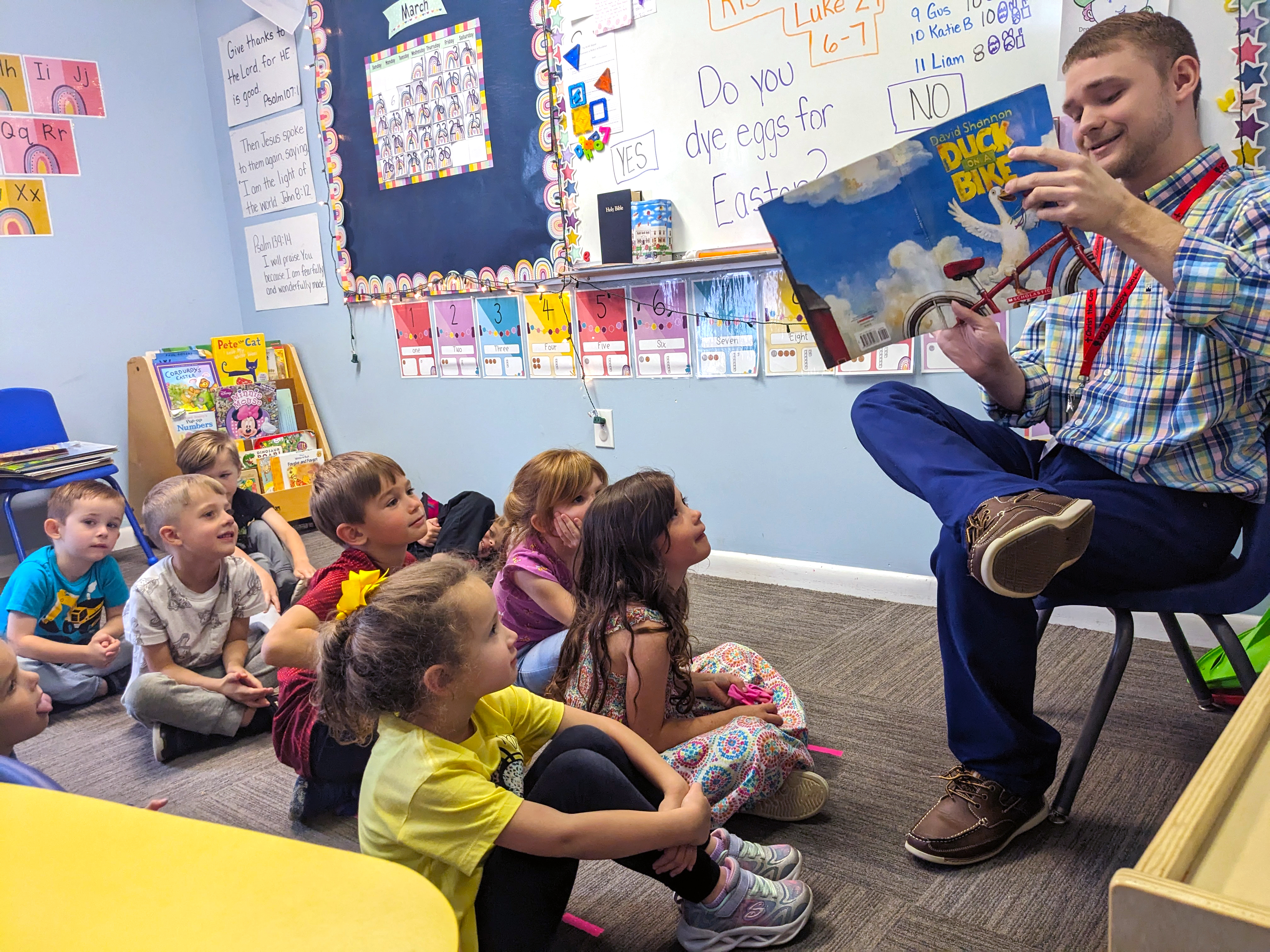 A student teacher reads a book to a group of children.