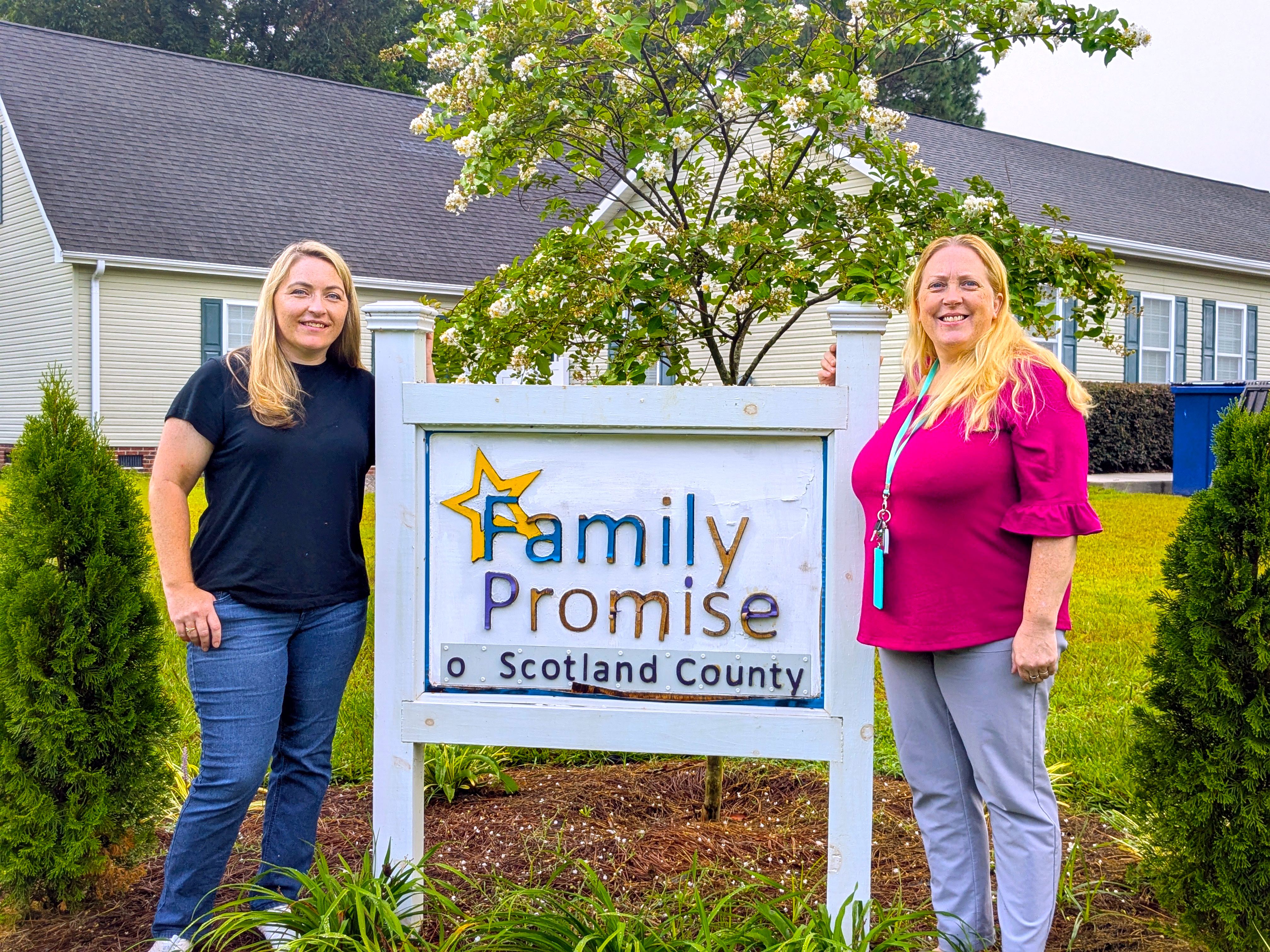 Tina and Kristy stand beside Family Promise sign in front of the home.