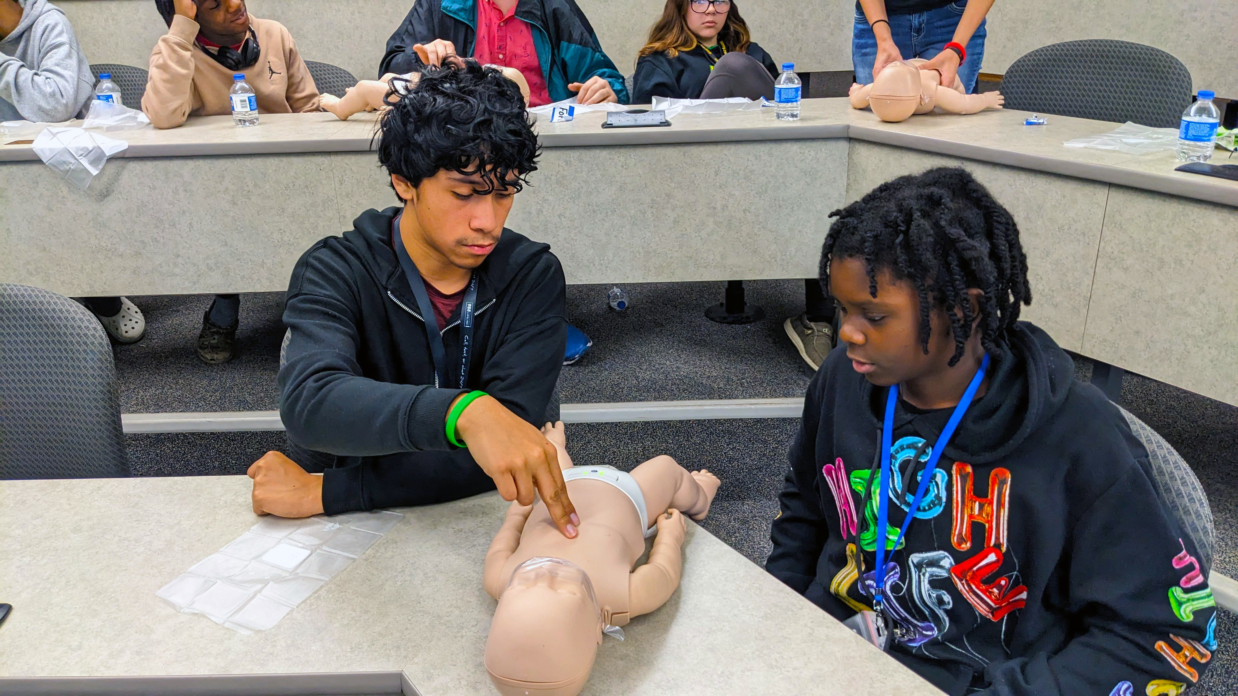 Two students prepare to perform CPR on a mannequin.