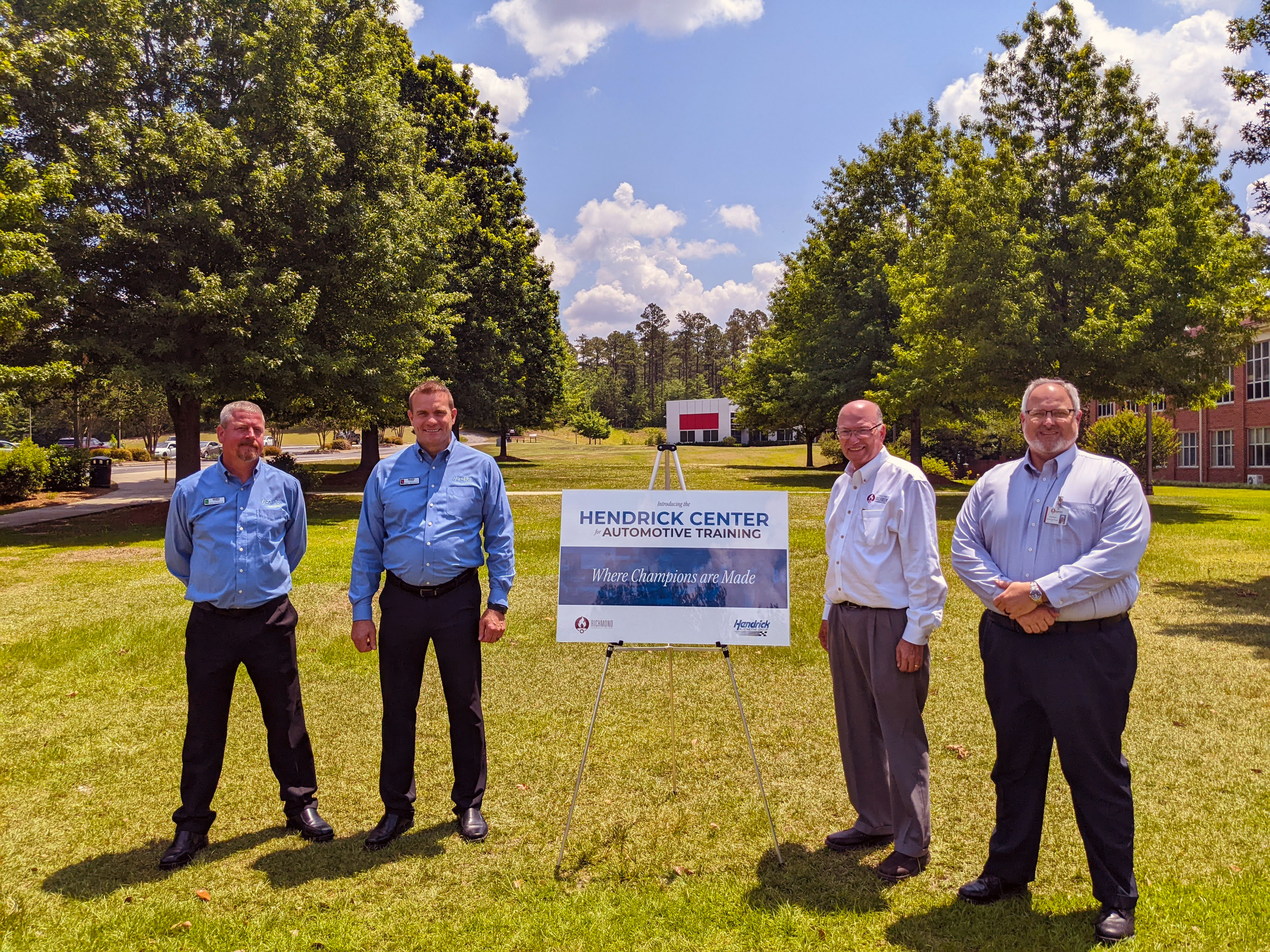 College leaders and Hendrick team members stand beside a sign for the Hendrick Center for Automotive Training on the future site of the facility.