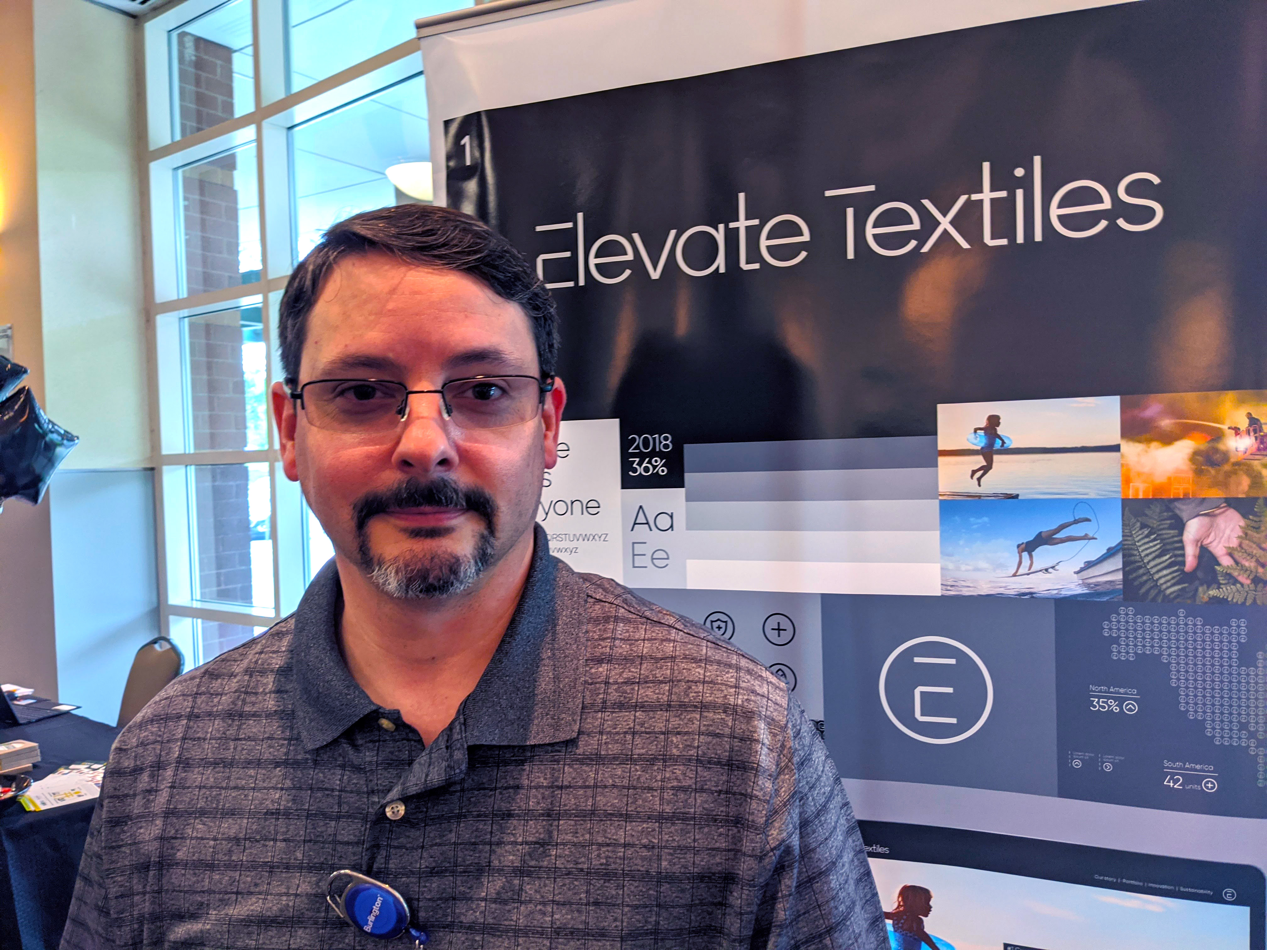 John Phillips stands in front of a banner for Elevate Textiles