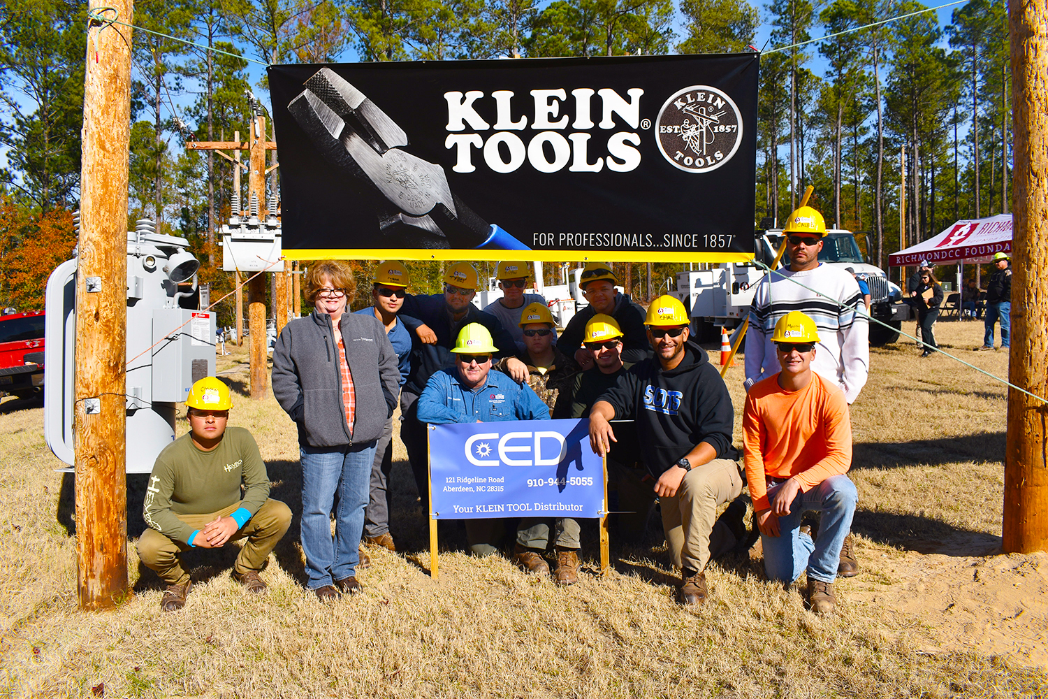 Electric lineman students stand with sales rep by Klein Tools sign