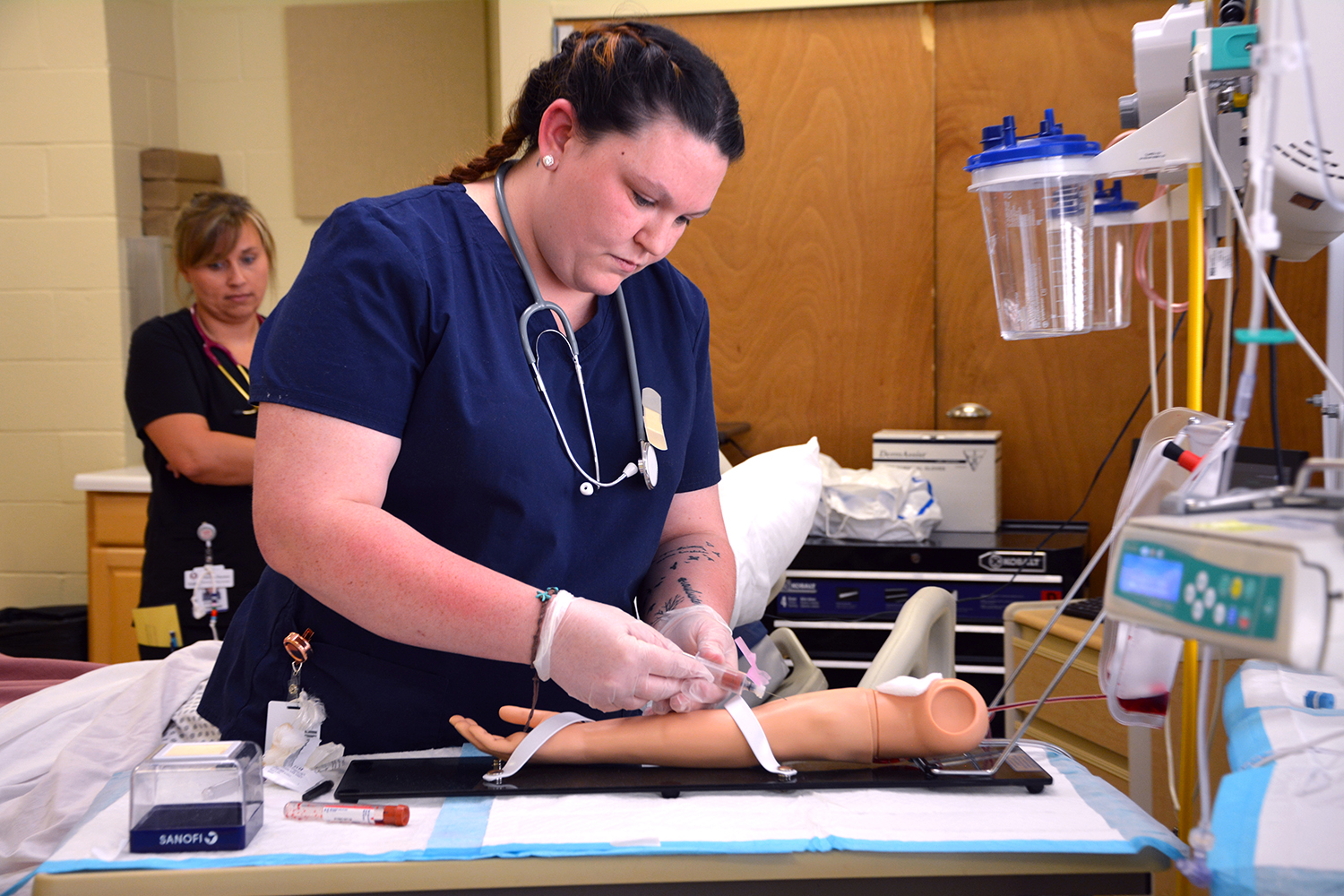 A medical assisting student draws blood from a fake arm