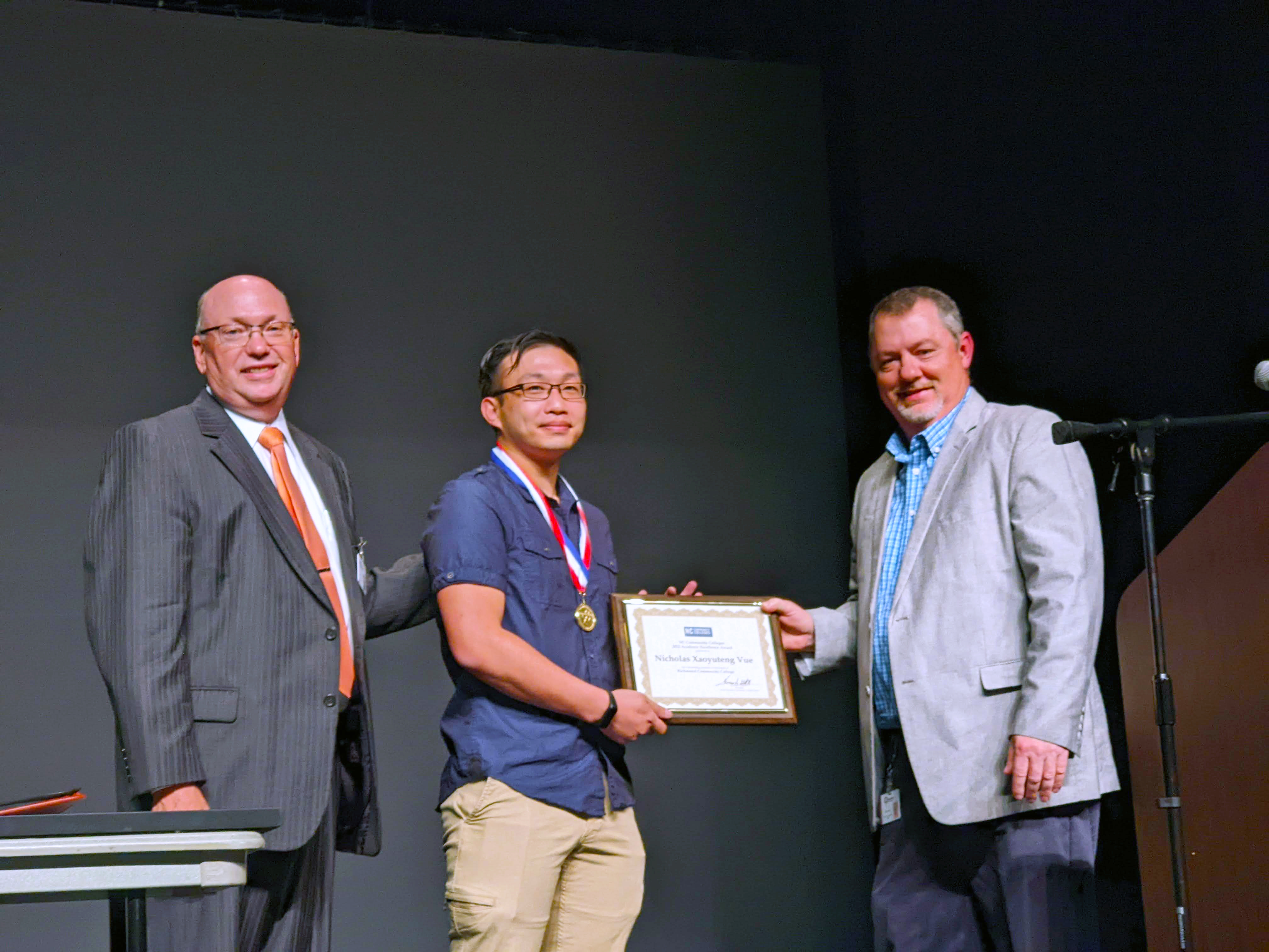 Nicholas Vue accepting his award on stage with college leaders