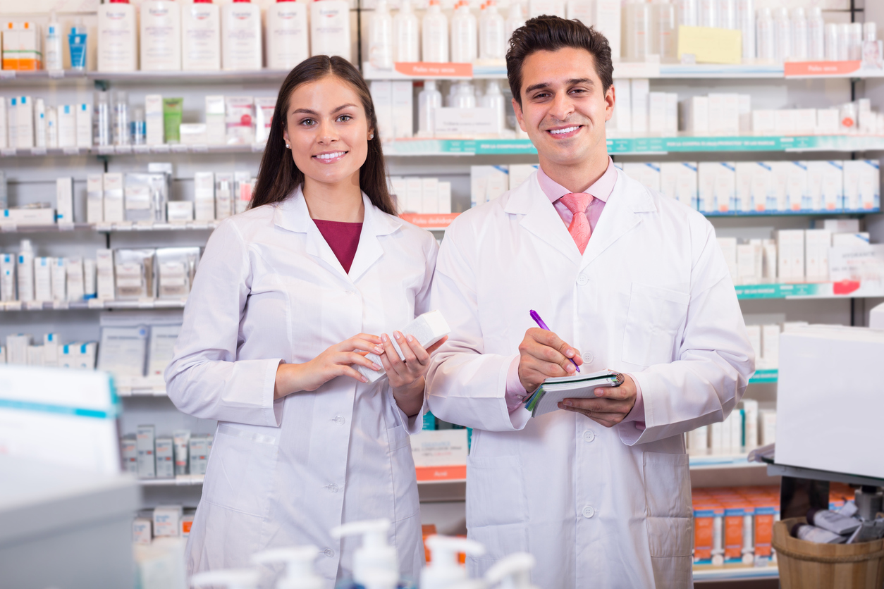 Two pharmacy technicians stand behind a pharmacy counter